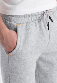 Graue Sweatpants mit strukturiertem Finish, ausgestattet mit einem elastischen Bund, Kordelzug und Taschen, die mit orangefarbenen Akzenten versehen sind.