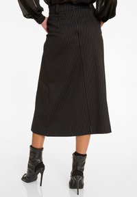 Schwarzer, gestreifter Midirock mit geradem Schnitt, ausgestattet mit einem Taillenbund, und kombiniert mit schwarzen, hochhackigen Stiefeletten.