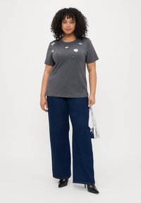 Grå bomull T-skjorte med korte ermer, prydet med blomsterdekorasjoner og paljetter på brystet, balansert med vide, mørkeblå jeans.