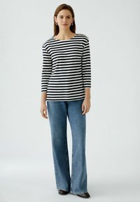 Gestreiftes Langarmshirt in Schwarz und Weiß mit einem Bootsausschnitt und dekorativen Knöpfen an der Schulter, kombiniert mit weit geschnittenen blauen Jeans.