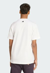 White cotton t-shirt with a round neck and short sleeves. Features a small black Adidas logo on the upper back. Plain design, relaxed fit.
