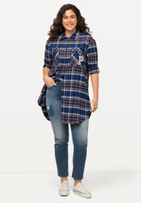 Blauwe en rode geruite overhemdbloes met twee borstzakken, met een geborduurde letter "P," gecombineerd met verouderde lichtblauwe jeans en witte sneakers.