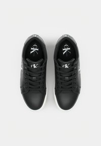 Zapatillas de cuero negro con suela de goma blanca, cuentan con cordones negros, logo en la lengüeta y detalles sutiles en los laterales.