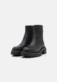Botas de tobillo de cuero negro con costados elásticos, que cuentan con una suela gruesa y un pespunte plateado a lo largo del borde. Textura suave en general.