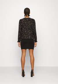 Camisa preta de manga longa com um padrão abstracto texturizado em bronze, combinada com uma saia mini preta ajustada e sandálias pretas de salto bloco.