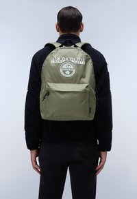 Zaino verde oliva con una tasca frontale con zip, caratterizzato da un logo circolare e del testo. Realizzato in tessuto resistente, sagomato con spalline curve per maggiore comfort.