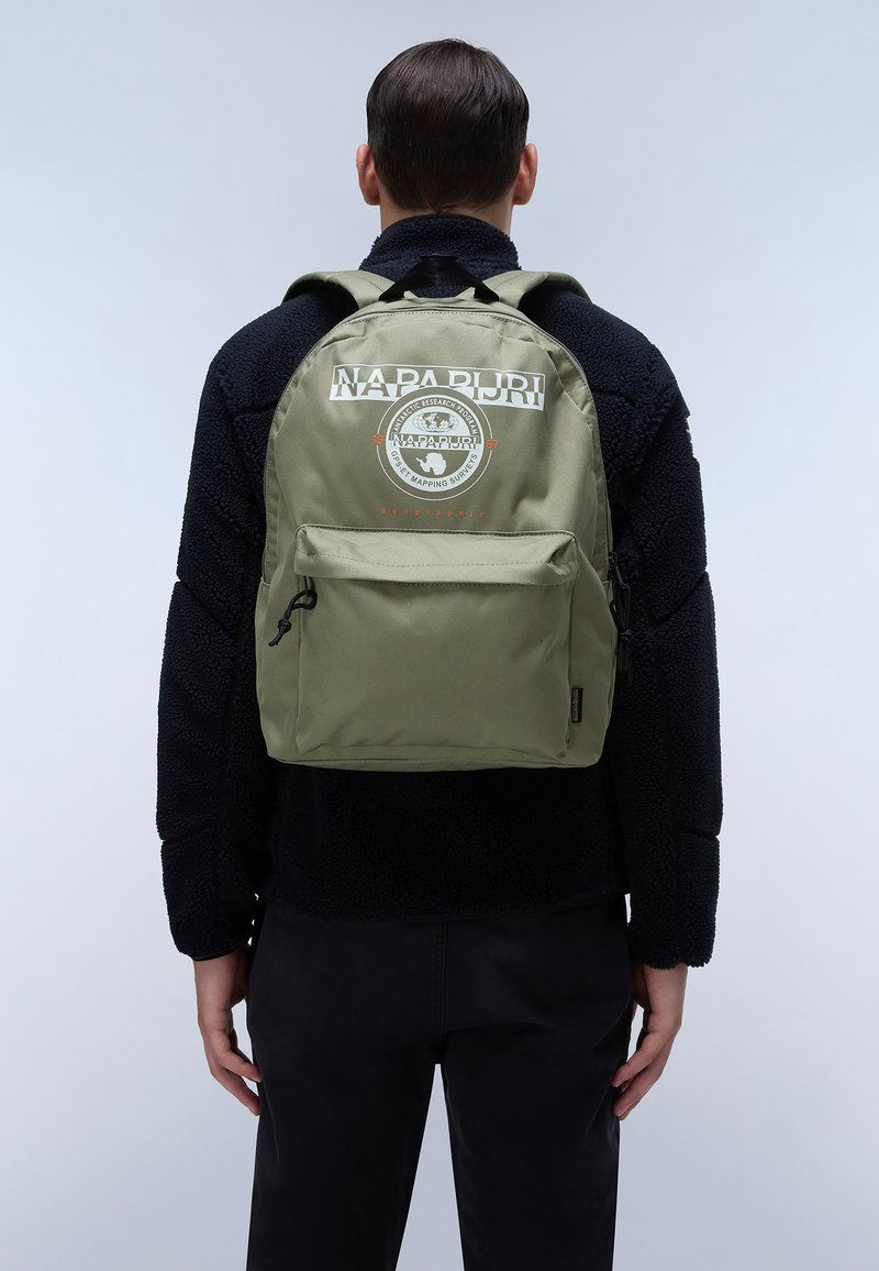 Zaino verde oliva con una tasca frontale con zip, caratterizzato da un logo circolare e del testo. Realizzato in tessuto resistente, sagomato con spalline curve per maggiore comfort.