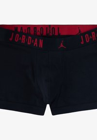 Boxer in cotone neri con una fascia elastica rossa che presenta la scritta "JORDAN" e un piccolo logo. Tessuto liscio, design aderente e lunghezza corta dei pantaloni.