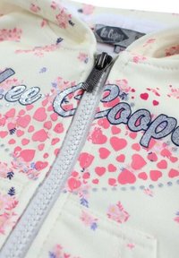 Sweat à capuche jaune pâle à fermeture éclair, avec des motifs de cœurs et de fleurs, un texte brodé argenté "Lee Cooper" et une fermeture éclair texturée.