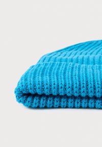 Strikket lue i lys blå, med ribbestruktur og rullet kant. Laget av mykt materiale, som viser en lett og koselig design.