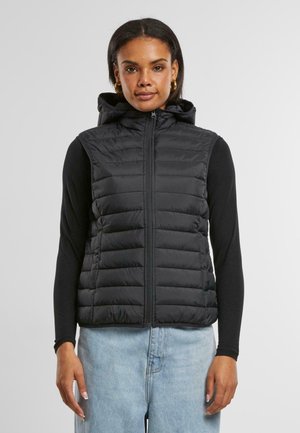 Vesta puf tip neagră cu fermoar frontal și glugă. Design capitonat cu o textură netedă. Purtați peste un top negru cu mânecă lungă și blugi de culoare albastru deschis.
