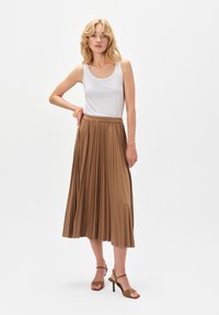 Brąskowa spódnica midi w plisy o gładkiej fakturze i elastycznej talii, w połączeniu z białym topem na ramiączkach i brązowymi szpilkami.