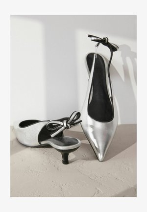 Sølvfarvede, patenterede læder slingback-sko med spidse tæer og lav hæl. Har en sort sløjfe-ornament på hælen.