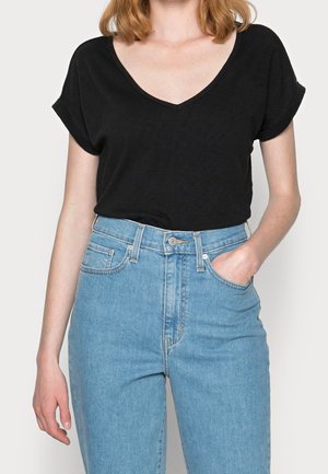 Czarny T-shirt z dekoltem w serek, wykonany z bawełny, z podwiniętymi krótkimi rękawami. W zestawie z jasnoniebieskimi, wysokim stanem jeansami z przodu z kieszeniami.