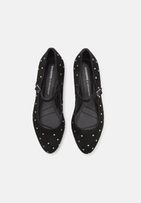 Ballerines en suede noir avec un bout pointu, présentant une sangle et des clous en argent harmonieusement espacés sur la surface. Semelle intérieure texturée visible.