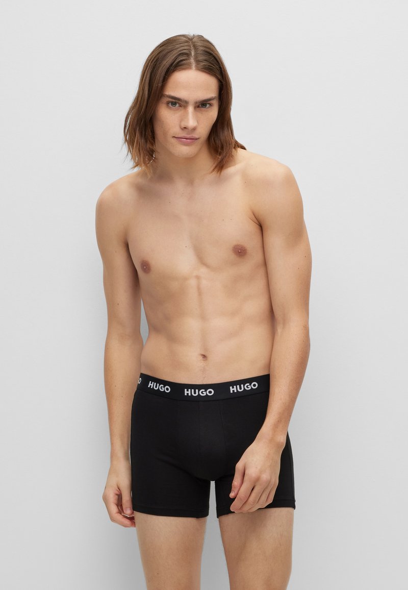 Zwarte boxershorts met een geborduurd logo op de tailleband. De stof lijkt glad, en het ontwerp is aansluitend, geschikt voor casual kleding.