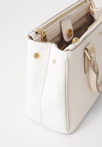 Sac à main synthétique blanc avec une texture lisse, quincaillerie dorée et fermeture à double zip. Présente une forme structurée et des poignées courtes.