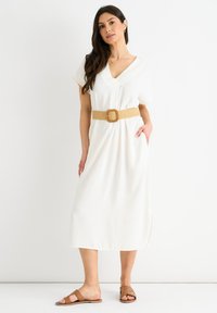 Abito midi bianco con maniche corte e scollo a V, cinato in vita con una cintura intrecciata color sabbia. Indossato con sandali piatti marroni.