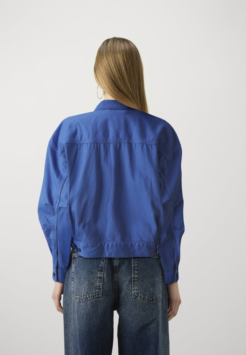 Blaue Jeansjacke mit lockerer Passform, ausgestattet mit einem Kragen, Knöpfen an den Ärmelbündchen und einer glatten Textur, kombiniert mit hoch-taillierten Jeans.