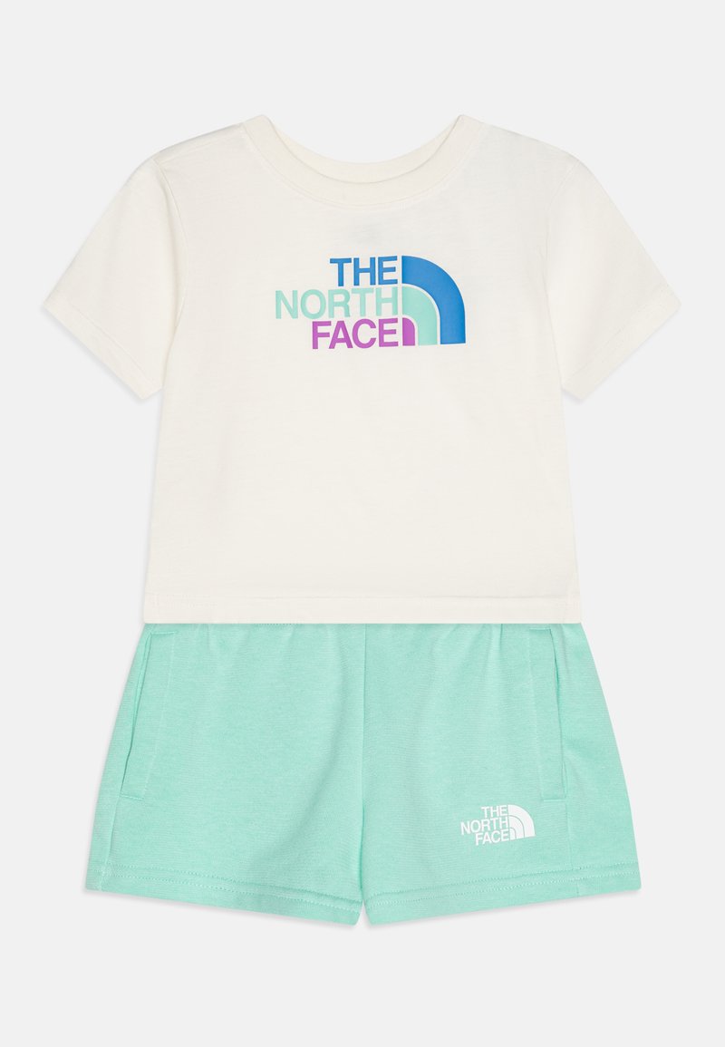 Camiseta de algodón color crema de mangas cortas con un logo azul y morado, combinada con pantalones cortos verde menta con bolsillos laterales y un logo a juego.