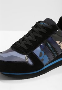 Baskets en daim noir et synthétique avec des motifs graphiques bleus et violets, des lacets noirs et un accent bleu le long de la semelle.