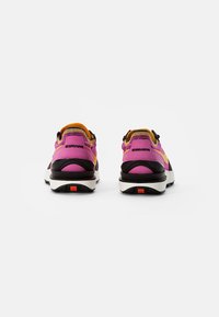 Paire de chaussures de sport roses et orange vues de dos, avec des semelles noires et blanches et de petits détails orange sur les talons.