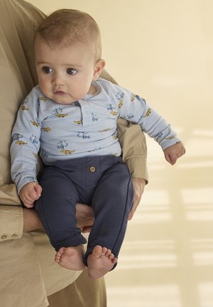 Lyseblå langærmet heldragt med dyreprints, kombineret med mørkeblå bukser med en knap. Blød tekstur, tætsiddende pasform og op rullede ærmekanter.