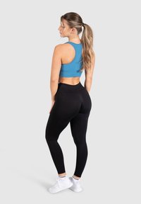 Top corto de canalé azul y leggings negros. La parte superior presenta un diseño de espalda al descubierto, mientras que los leggings tienen una textura suave, combinados con zapatillas blancas.