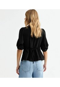 Svart blus med puffärmar, samlad midja och knytdetalj bak. Kombinerad med ljusblå högmidjade jeans. Texturerad tyg.