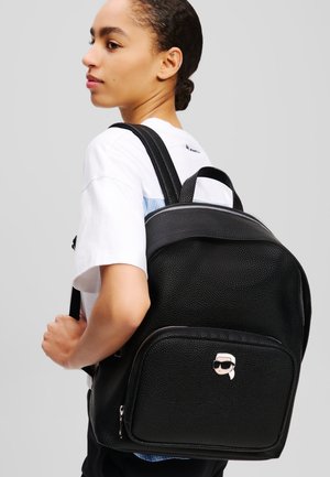 Sac à dos en cuir texturé noir avec une poche avant ornée d'un design de visage de dessin animé. Bretelles ajustables et poignée supérieure pour un transport facile.