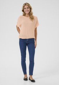 Jasno brzoskwiniowa bluzka z krótkim rękawem zestawiona z ciemnoniebieskimi skinny jeansami i czarnymi płaskimi butami. Bluzka ma luźny krój i miękką teksturę.
