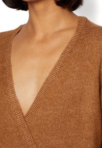 Tan v-ringad ulltröja med en mjuk textur, märkbar ribbad detalj längs halslinningen och en inslaget design.