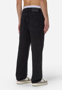Czarne dżinsy o szerokich nogawkach, wykonane z denimu, z wysokim stanem, dwiema tylnymi kieszeniami i prostą czarną metką na pasku.