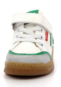 Zapatilla blanca con acentos en verde y gris, que presenta una correa de Velcro, cierre de cordones y suela de goma. Materiales texturizados utilizados.