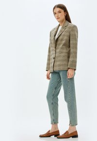 Rutig blazer i beige och bruna nyanser med slag, parat med ljusblå raka jeans och bruna loafers.