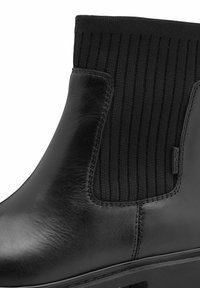 Botte de cheville en cuir noir dotée de panneaux élastiques sur les côtés, d'une texture lisse et d'un talon légèrement rehaussé. Design minimaliste avec des coutures ton sur ton.