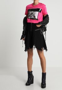 Ljust rosa t-shirt med grafiskt tryck och svarta detaljer, kombinerad med en svart denimkjol med fransade kanter och dragkedjefickor. Kraftiga svarta plattformskängor.