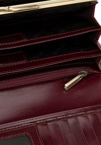 Portafoglio in pelle bordeaux con multiple scomparti, chiusura in metallo dorato, sezione con zip e dettagli testurizzati. Il tessuto interno presenta il marchio.
