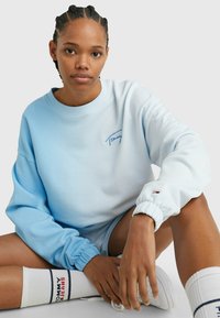 Sudadera azul claro con puños acanalados, que presenta el logotipo bordado de "Tommy". Textura suave y corte relajado. Calcetines blancos con acentos de logotipo.