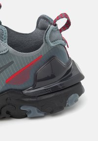 Sportskor med en grå meshev uppdelning, röda detaljer och en flexibel svart gummisula med texturerat mönster för grepp.