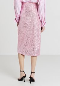 Donna che indossa una gonna midi di paillettes rosa, una maglietta a righe rosa a maniche lunghe e sandali neri con tacco alto, vista da dietro.