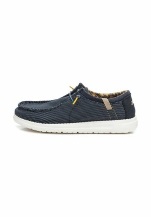 Zapato slip-on de malla en color marino con suela de goma blanca, con cordones amarillos, forro interior texturizado y acentos marrones en el talón.
