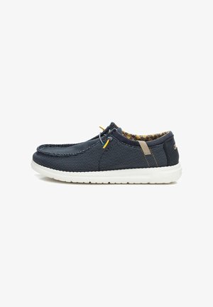 Zapato slip-on de malla en color marino con suela de goma blanca, con cordones amarillos, forro interior texturizado y acentos marrones en el talón.