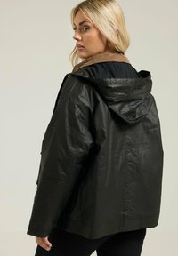 Veste en cuir noir avec capuche, dotée d'un col en velours côtelé marron et d'une coupe décontractée. La surface présente une texture légèrement brillante.