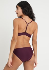 Bikini-Set in dunklem Burgundy, mit einem eleganten Design, dünnen Trägern und einem Verschluss auf der Rückseite, hergestellt aus glattem, dehnbarem Stoff.