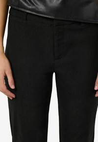 Crne hlače od glatkog materijala, s bočnim džepovima i klasičnim krojem. Pojas je jednostavan bez vidljivih elemenata ili ukrasa.