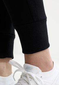 Svarta sweatpants med ribbade muddar, kombinerade med en vit sportskor försedd med texturerad tyg och en framträdande logotyp på sidan.