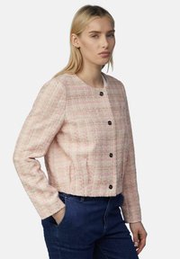 Geweven rozenkrans en crèmekleurige cropped jacket met een gestructureerde afwerking, ronde halslijn en zwarte knopen, gecombineerd met donkere spijkerbroeken.