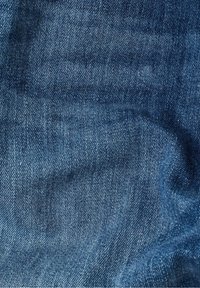 Gros plan d'un tissu denim bleu montrant la texture tissée et de légers plis sur le matériau.