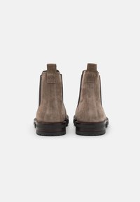 Bottes Chelsea en daim marron avec panneaux latéraux élastiques, languettes de traction et semelles robustes en caoutchouc noir, présentant un design épuré et minimaliste.
